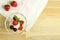 Ice cream dessert with strawberries and cherries in a gourd on a wooden table next to scattered berries.