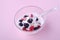 Ice cream with raspberry, blackberry berries with spoon in glass bowl on pink background