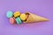 Ice cream waffle cone with colorful macaron or macaroon on violet purple background top view. Colorful candy colors