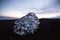 Ice crystal part piece iceberg glacial fragment on black sand ocean waves sunset Diamond Beach Jokulsarlon South Iceland