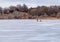 Ice fishing; Frozen lake surface in winter with two ice fishermen preparing for drilling.