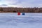 Ice fishing; Frozen lake surface in winter with two ice shanties on the frozen lake surface. 