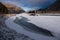 Ice-hole in ice-covered river on the background of a colorful sunrise and high rocks, Altai mountains