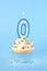 Iced birthday cupcake with with lit number 0 candle