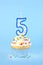 Iced birthday cupcake with with lit number 5 candle