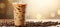 Iced coffee in plastic cup on beige bokeh background with coffee seeds and text space