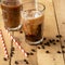Iced iced coffee in large transparent glasses, poured over milk, with coffee beans on a wooden background, summer cooling drink