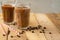 Iced iced coffee in large transparent glasses, poured over milk, with coffee beans on a wooden background, summer cooling drink