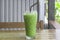 Iced matcha latte or condensed milk-added green tea in transparent glass with black straw on wooden table served at coffee shop