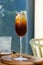 Iced mix fruit juice with black cold brew coffee in wine glass on wooden table. Concept fusion drink menu summer drink