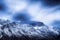 Iced over mountains peaks and cliffs against cold blue sky and feather clouds, created with Generative AI