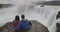 Iceland Travel Couple sitting relaxing in nature hike by Iceland waterfall