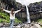 Iceland. Woman enjoying majestic Svartifoss waterfall. Female is visiting famous tourist attraction of Iceland