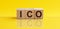 ICO abbreviation stands for Initial Coin Offering on wooden blocks, yellow background. Cryptocurrencies concept