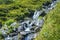 An icy river flows down from the mountains through rocks and vegetation