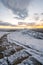 Icy snow covered winding stone footpath path way leading up mountain side as sun starts to come above horizon at sunrise winter