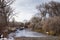 Icy stream with bare deciduous trees and overcast skies.