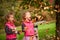 Identical twins having fun with autumn leaves, blond cute curly girls, happy family, beautiful girls in pink jackets