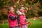 Identical twins having fun with autumn leaves, blond cute curly girls, happy family, beautiful girls in pink jackets