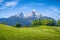 Idyllic alpine landscape with green meadows, farmhouses and snow-capped mountain tops