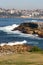 Idyllic and amazing seaside landscape of jagged shore with rocks, white rushing sea waves, hillside buildings in Sydney, Australia