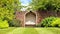 Idyllic garden with bench under trees, next to red brick wall .