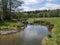 Idyllic landscape of winding river stream meander at lush green meadow with deciduous tree forest, blue sky backgound