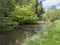 Idyllic landscape of winding river stream meander at lush green meadow with deciduous tree forest, blue sky backgound