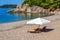 Idyllic scene of deck chairs under an umbrella on a clean beach in the hot afternoon sun.