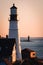 Idyllic scene of a lighthouse by the ocean at sunset, silhouettes of nearby buildings in background