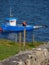 Idyllic scene of a small blue boat near a grassy green hillside, overlooking a peaceful lake