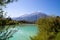 Idyllic shore landscape with pebble beach, blue water, flowers and mountains