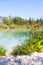 Idyllic shore landscape with pebble beach, blue water, flowers and wood