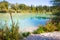 Idyllic shore landscape with pebble beach, blue water, flowers and wood