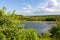 Idyllic summer landscape with river, hill, green trees, blue sky, and white clouds. Natural warm light