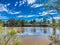 Idyllic tranquil muddy dam near lush trees under a blue sky in Emmaville, Australia