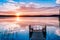 Idyllic view of the long pier with wooden bench on the lake. Sunset or sunrise over the water