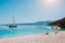 Idyllic white beach with umbrellas on lazy summer day. Sailing boat on calm crystal clear water