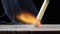 Igniting a spark from a match by rubbing it against a sulfur-coated box. On a black background close-up in a macro.