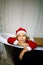 Iittle girl in Santa Ð¡hristmas hat is sitting in a bathtub