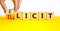 Illicit or elicit symbol. Businessman turns wooden cubes and changes the concept word Illicit to Elicit. Beautiful yellow table