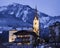 Illuminated Catholic church St. Margaretha with street, lights, mountains and forest in Kaprun Austria at blue hour