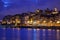 Illuminated city buildings and boats reflecting colorful lights into Douro River along waterfront in Porto, Portugal