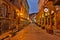 Illuminated cobbled street with light reflections on cobblestones in old historical city by night. Dark blurred