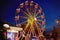 Illuminated ferris wheel in amusement park at a night city