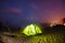 Illuminated green camping tent under stars at night