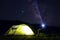Illuminated green tent with man sitting near and mountains silhouette and many stars background. Hiking, tourism concept. Adventur