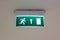 Illuminated green and white exit sign on the ceiling in a public place.