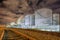 Illuminated oil refinery at night with large silos and rail tracks