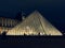 Illuminated pyramidal-shaped skylight of the Louvre Museum, at night in Paris, surrounded by people